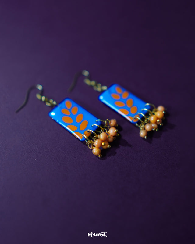 Sandhyaraag hook floral earrings in a close-up view, highlighting the vibrant blue base with scattered orange petal motifs and neatly dangled orange beads, creating a cheerful and artistic boho aesthetic — Muselot.