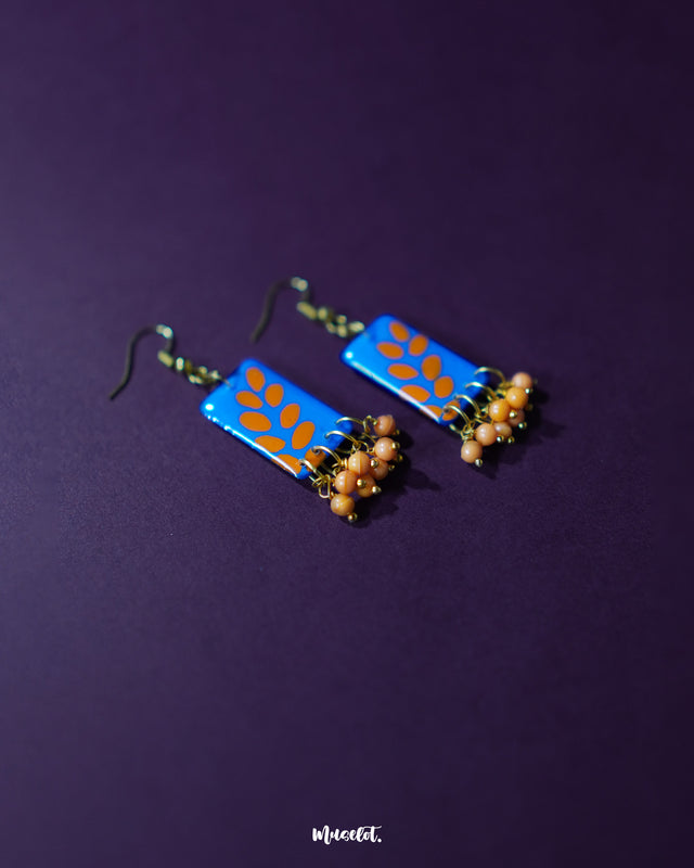 Sandhyaraag hook floral earrings displayed against a dark background, featuring a bold blue base adorned with scattered orange petal motifs and delicate orange bead danglers, blending playful color with handcrafted elegance — Muselot
