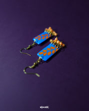 Sandhyaraag hook floral earrings displayed on a dark purple background, featuring blue rectangular drops with orange petal motifs and tiny orange bead accents, capturing the playful charm of handcrafted boho style — Muselot