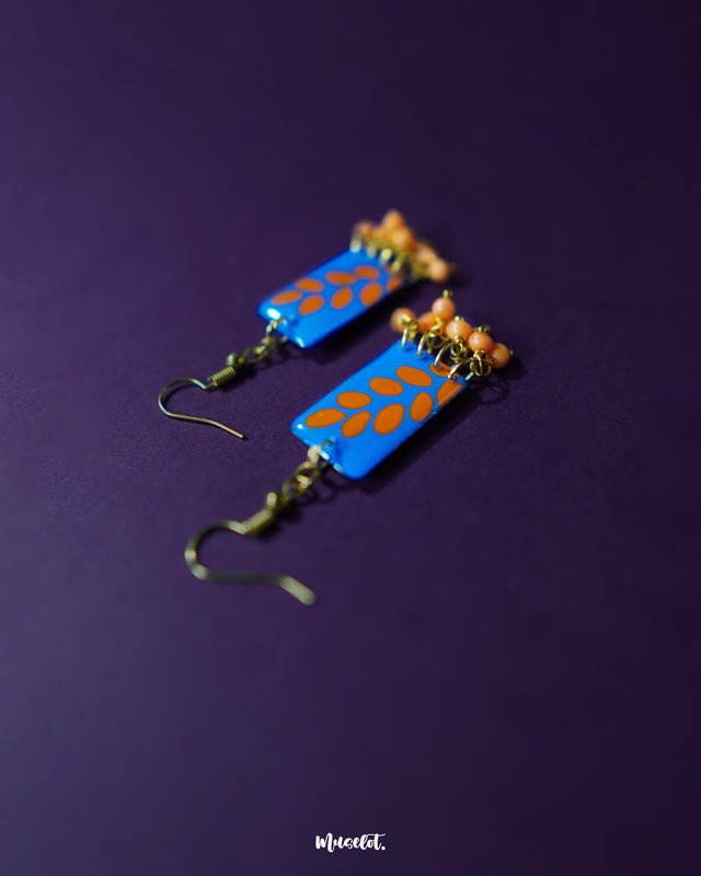 Sandhyaraag hook floral earrings displayed on a dark purple background, featuring blue rectangular drops with orange petal motifs and tiny orange bead accents, capturing the playful charm of handcrafted boho style — Muselot