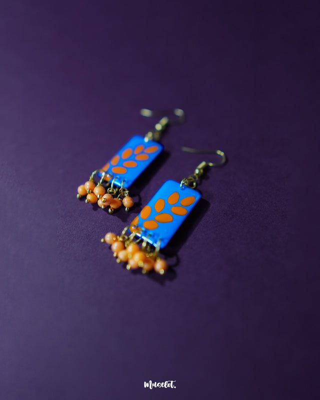 A close-up of Sandhyaraag hook floral earrings resting on a purple background, highlighting the intricate floral design, bold color contrast, and artisanal finish that give them a striking yet elegant appeal — Muselot