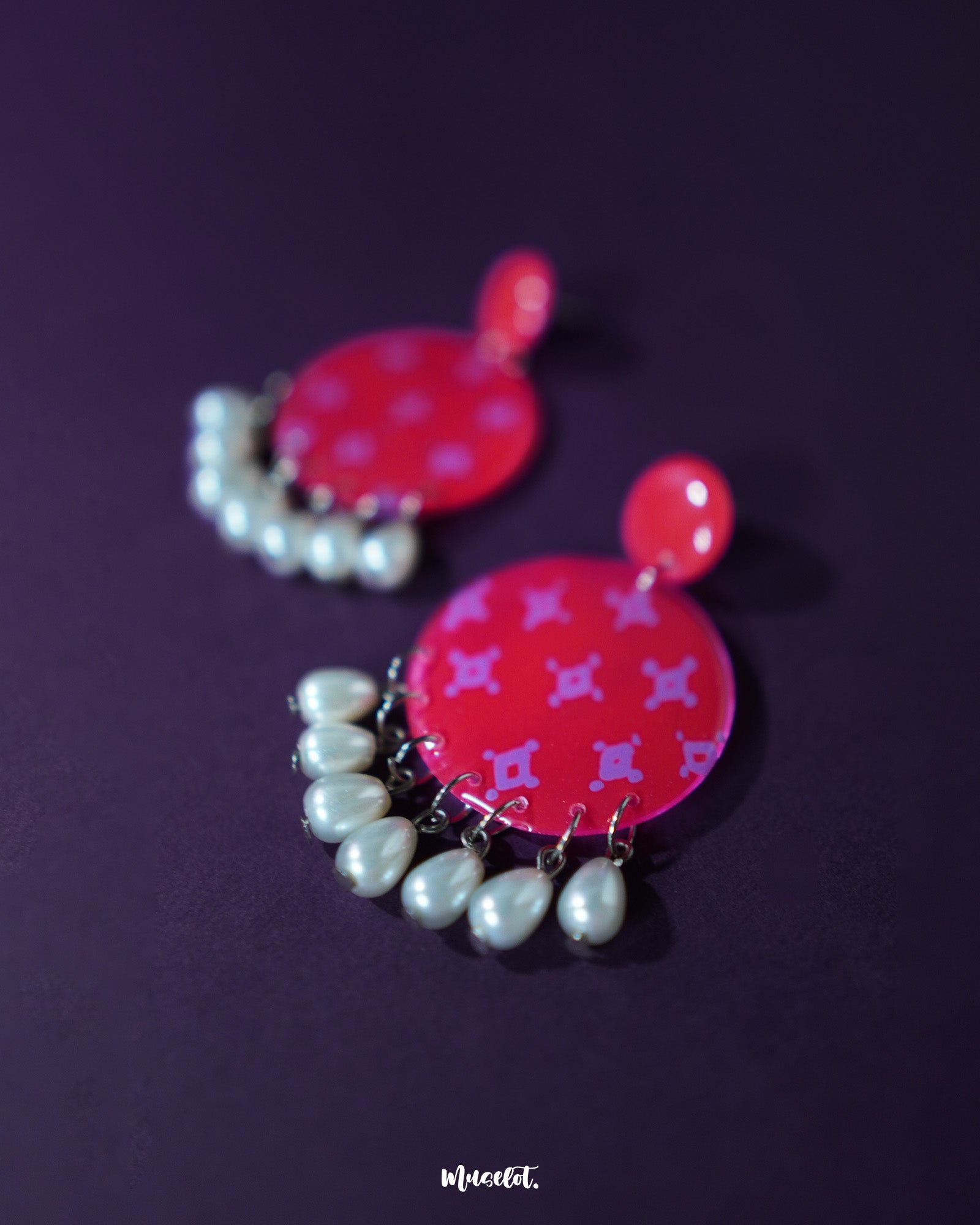 A closer look at the Shabnam pink pearl drop earrings placed on a soft beige background, showcasing the glossy finish of the round pink tops and the elegant white pearl-like drops hanging below, highlighting their handcrafted finesse and graceful appeal — Muselot.