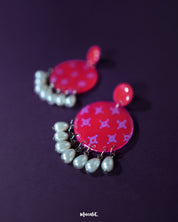 A closer look at the Shabnam pink pearl drop earrings placed on a soft beige background, showcasing the glossy finish of the round pink tops and the elegant white pearl-like drops hanging below, highlighting their handcrafted finesse and graceful appeal — Muselot.