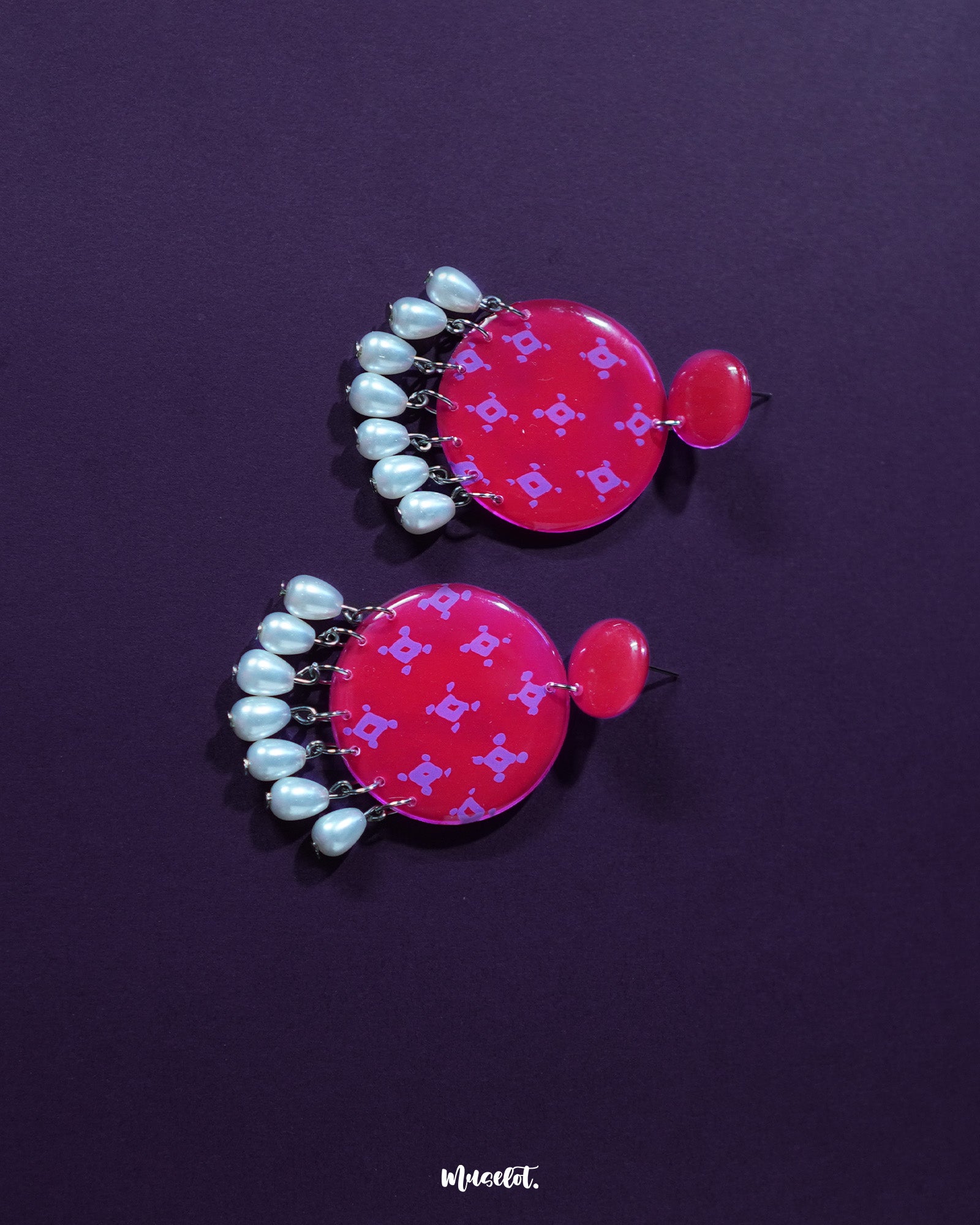 A close-up of the Shabnam pink pearl drop earrings resting on soft fabric, showcasing the glossy pink floral studs paired with elegant white pearl drops, highlighting their gentle shimmer and refined handmade detailing — Muselot.