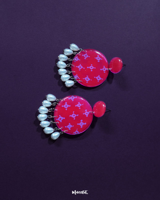 A close-up of the Shabnam pink pearl drop earrings resting on soft fabric, showcasing the glossy pink floral studs paired with elegant white pearl drops, highlighting their gentle shimmer and refined handmade detailing — Muselot.