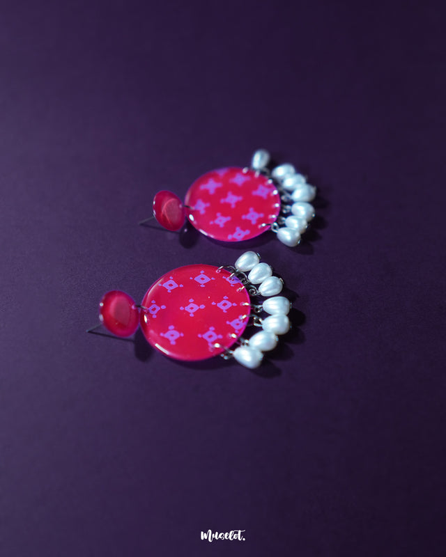 A Shabnam pink pearl drop earrings placed on a neutral surface, highlighting the glossy pink studs and dainty white pearl drops that together showcase a delicate fusion of charm and sophistication — Muselot.