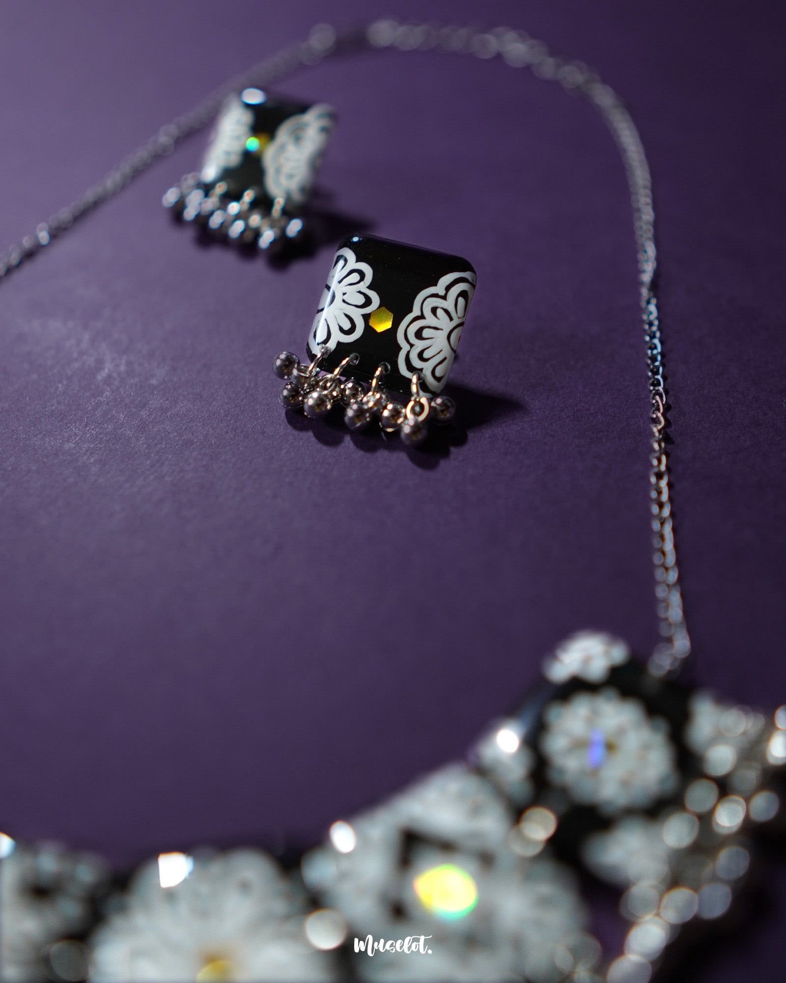 Close-up of the Shabnoor black floral jewelry set displayed on a neutral backdrop, showcasing the delicate hand-painted black flowers and fine detailing of the matching necklace and earrings — Muselot.