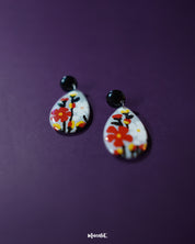 A shot of the Shafaq floral earrings placed against a rich purple background, showcasing their handcrafted floral design, delicate petal detailing, and elegant drop silhouette that adds a hint of traditional charm — Muselot