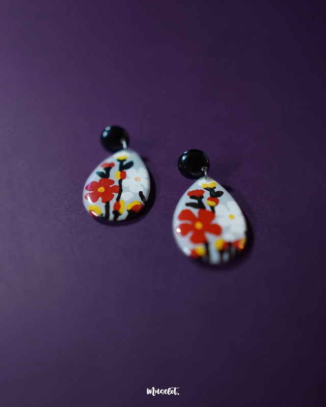 A shot of the Shafaq floral earrings placed against a rich purple background, showcasing their handcrafted floral design, delicate petal detailing, and elegant drop silhouette that adds a hint of traditional charm — Muselot