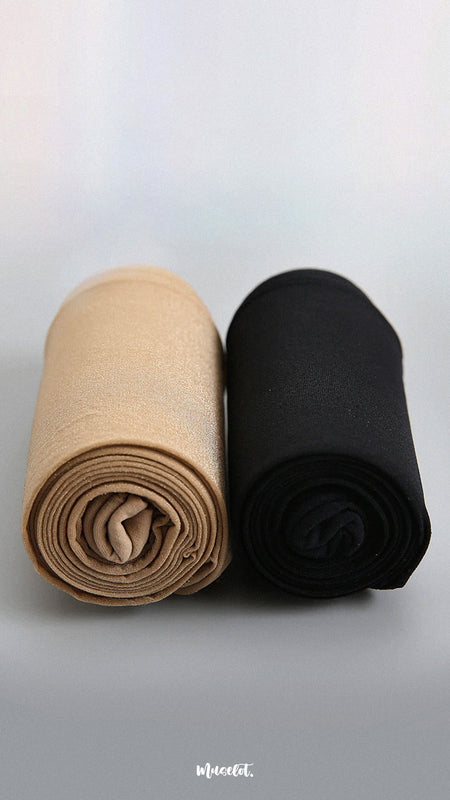 A pair of black and skin-colored silken touch stockings are rolled up and placed on a plain white background, showcasing their smooth texture and contrasting colors. The rolled-up design adds a dynamic touch, highlighting the flexibility and versatility of both stockings. -Muselot