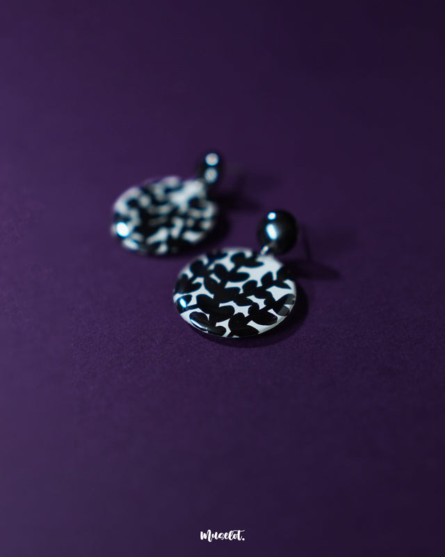 Siyahgul black floral stud earrings, placed against a dark purple background, featuring intricate floral patterns and a bold black finish that enhance their striking elegance and timeless charm — Muselot.