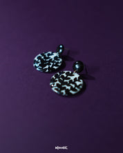 Siyahgul black floral stud earrings, framed by a rich purple backdrop, featuring delicate floral textures and a bold black hue that lend a touch of moody elegance and refined charm — Muselot.