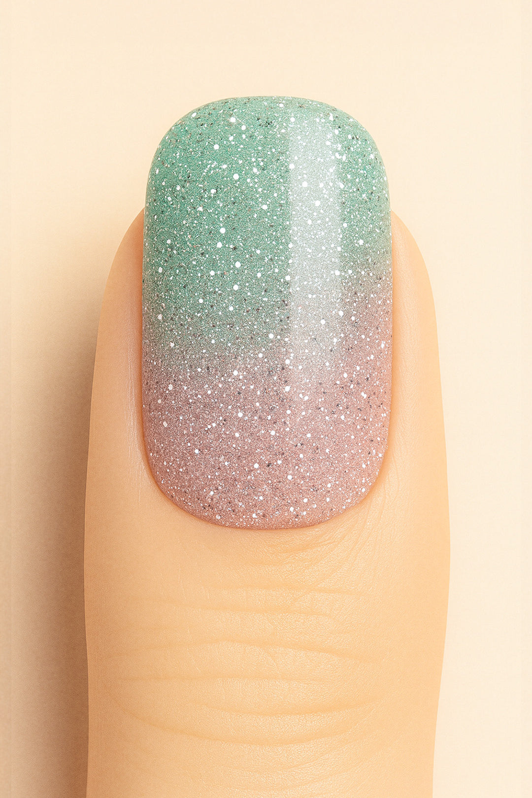 A close-up shot of a model’s finger wearing Snow Petal Ombre Nail Stickies, showcasing a delicate gradient design that blends soft blush pink into a minty green with sparkling silver glitter accents, highlighting the subtle shimmer and smooth ombre transition for an elegant winter-inspired nail art finish – Muselot.
