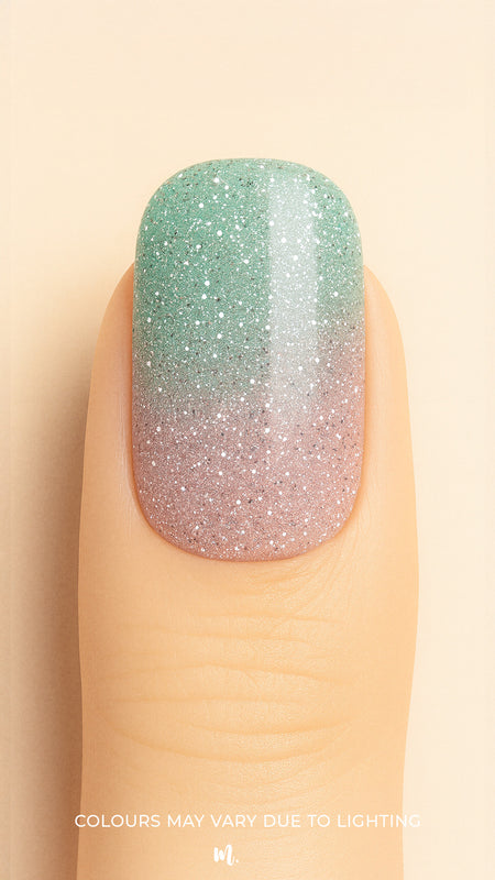 A close-up shot of a model’s finger wearing Snow Petal Ombre Nail Stickies, showcasing a delicate gradient design that blends soft blush pink into a minty green with sparkling silver glitter accents, highlighting the subtle shimmer and smooth ombre transition for an elegant winter-inspired nail art finish – Muselot.
