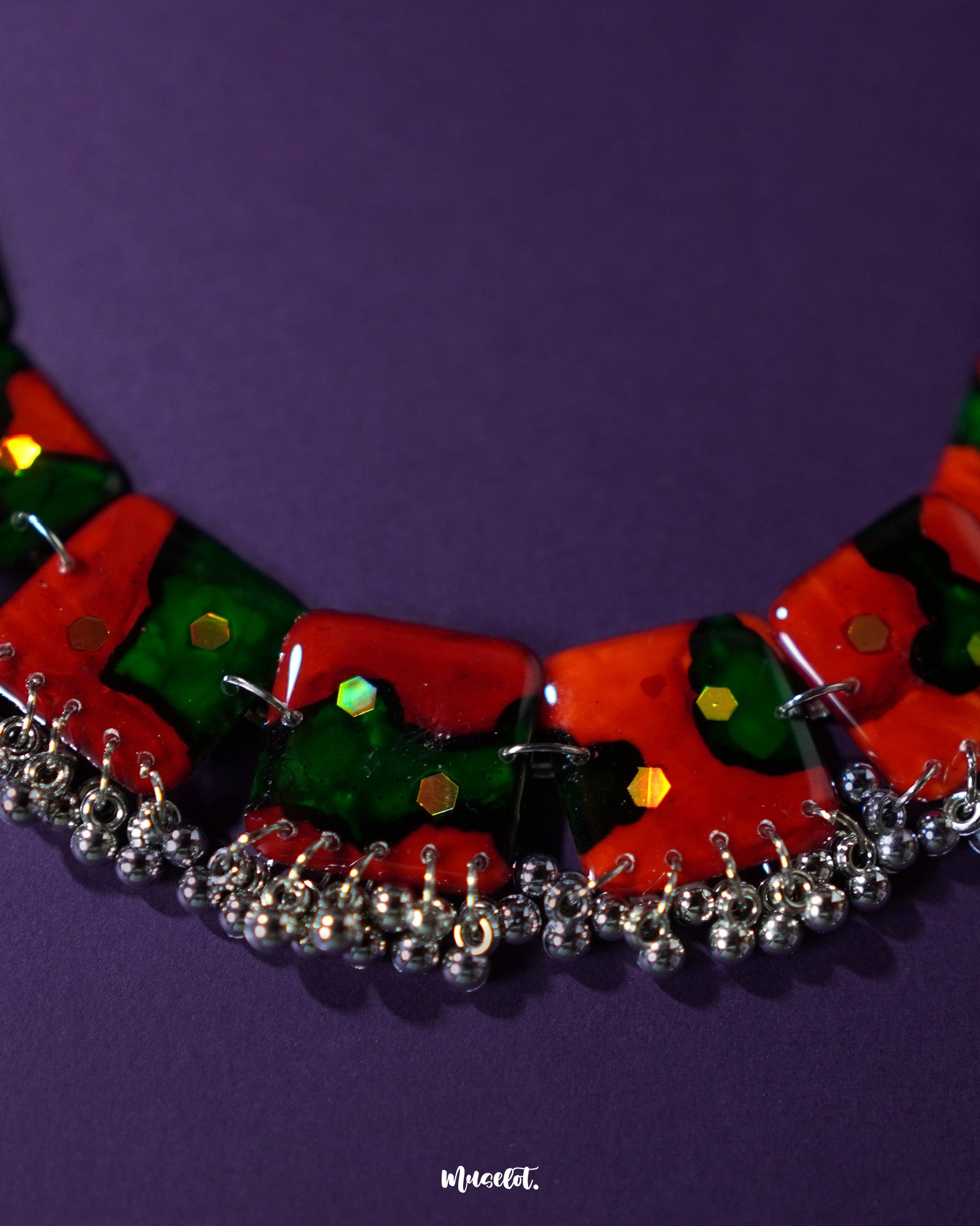 A stunning flat-lay of the Surkhbaagh handmade jewelry set featuring coordinated red and green earrings and necklace, adorned with intricate silver-toned charms — a harm onious blend of tradition and artistry — Muselot.