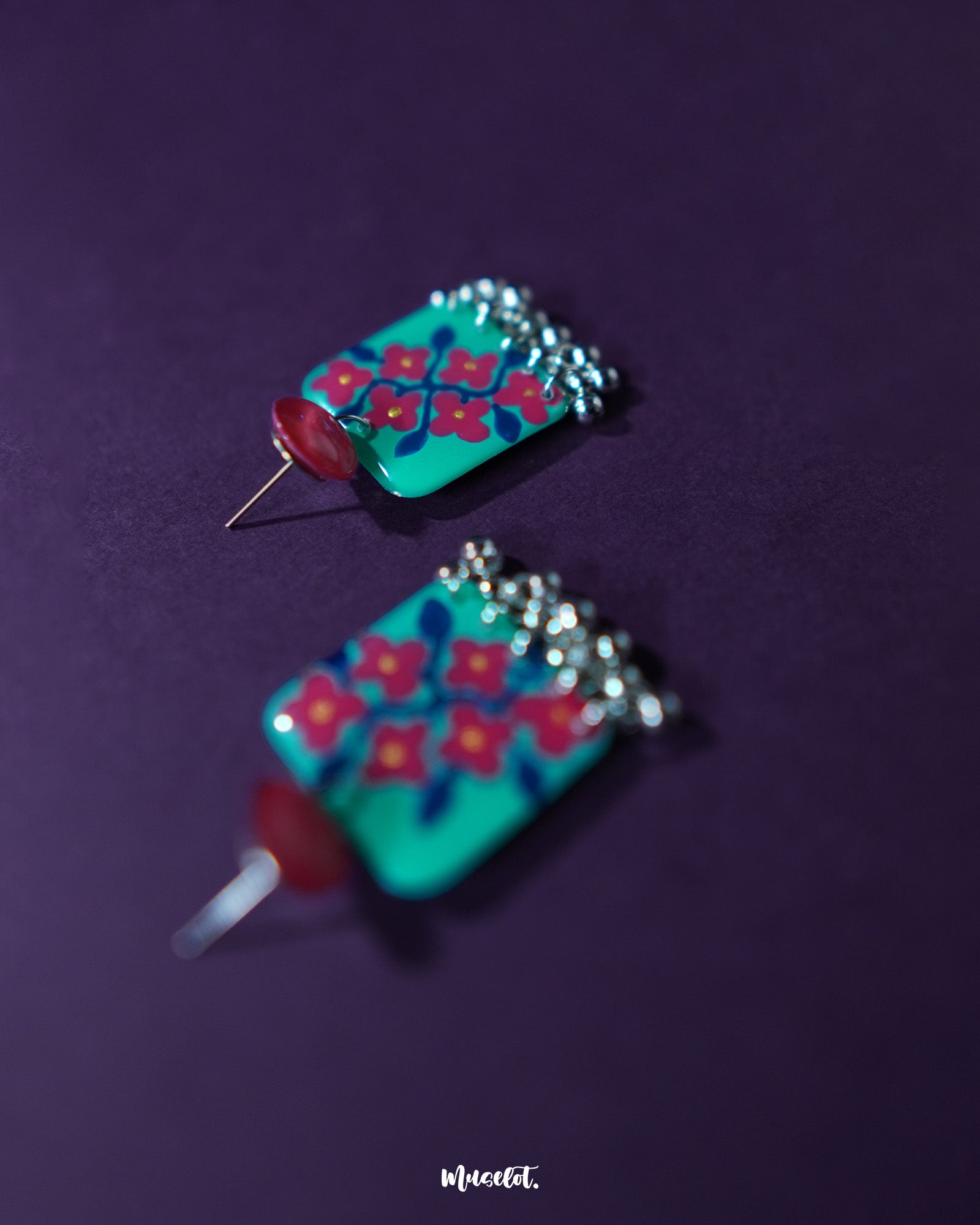 Close-up of Surkhili floral earrings displayed against a neutral backdrop, focusing on the intricate brushwork of the red flower petals and the polished finish of the silver ghungroos — Muselot.