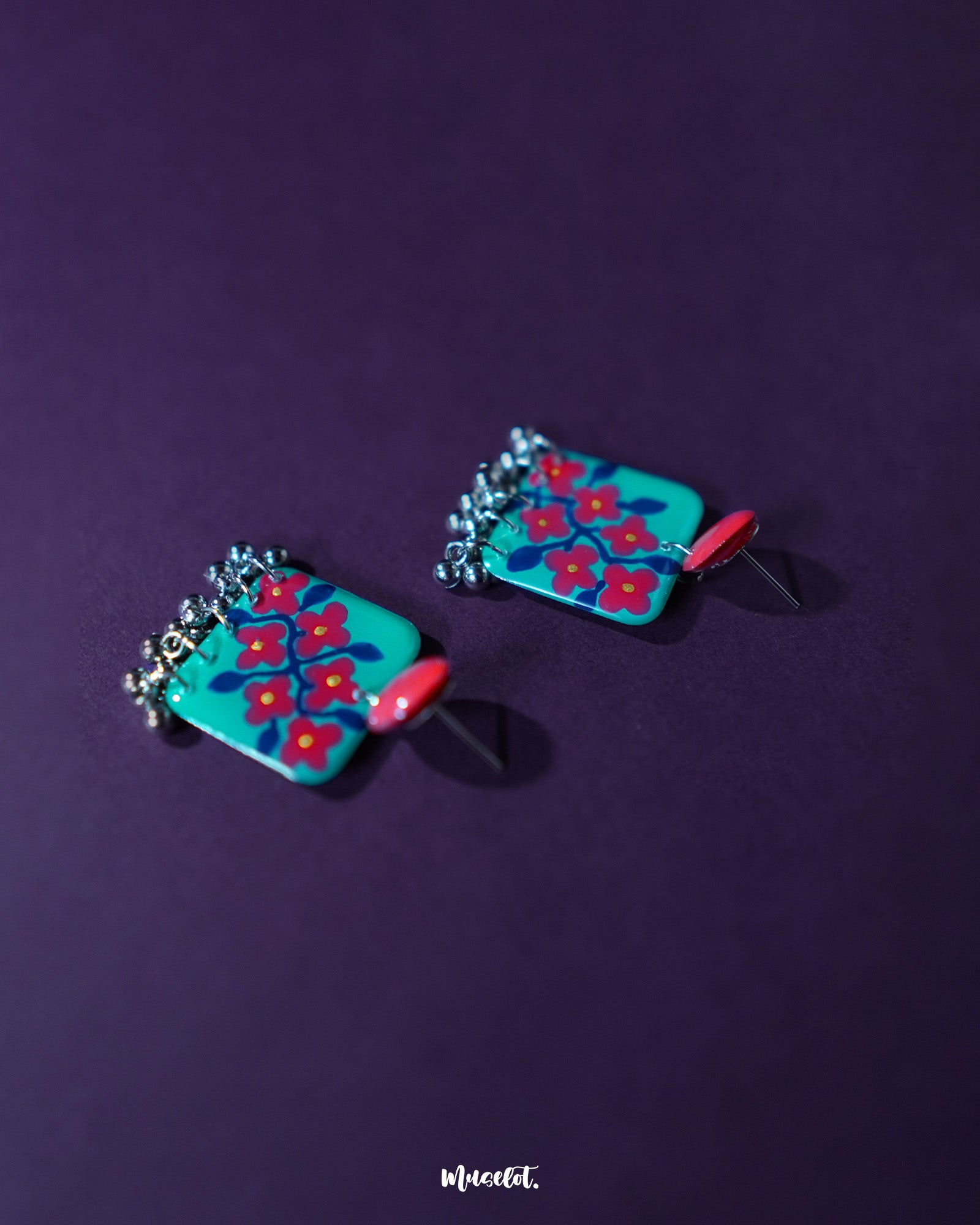 Pair of Surkhili floral earrings laid flat, highlighting the vibrant red blooms with delicately hand-painted petals and tiny dangling silver beads that add a charming ethnic flair — Muselot.