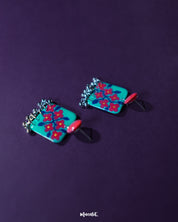 Pair of Surkhili floral earrings laid flat, highlighting the vibrant red blooms with delicately hand-painted petals and tiny dangling silver beads that add a charming ethnic flair — Muselot.