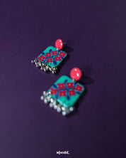 Surkhili floral earrings displayed on a textured backdrop, showcasing their vivid red floral design and silver-toned danglers that lend a festive, handcrafted elegance — Muselot.