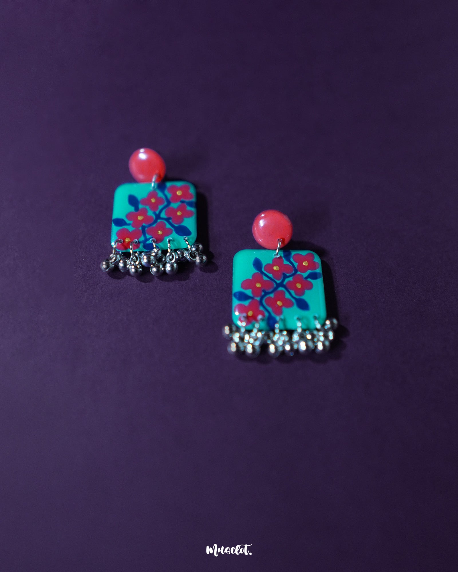 A pair of Surkhili floral earrings laid flat, featuring deep red floral elements and delicate silver details that bring out their ethnic charm and artisanal finish — Muselot.