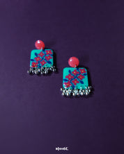 A pair of Surkhili floral earrings laid flat, featuring deep red floral elements and delicate silver details that bring out their ethnic charm and artisanal finish — Muselot.