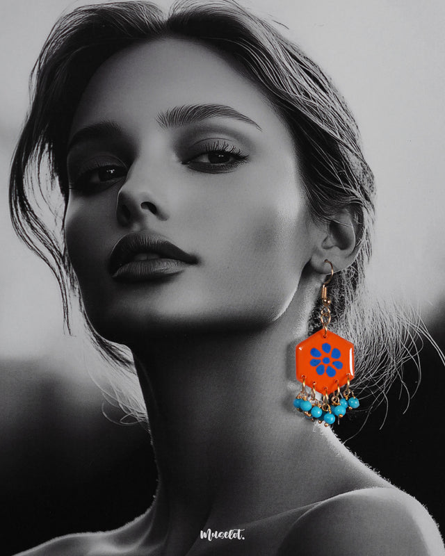 a model wearing Surkhshaam orange floral hook earrings, with vivid floral details and intricate design that beautifully complement the model's look, adding a touch of elegance and playfulness — Muselot.