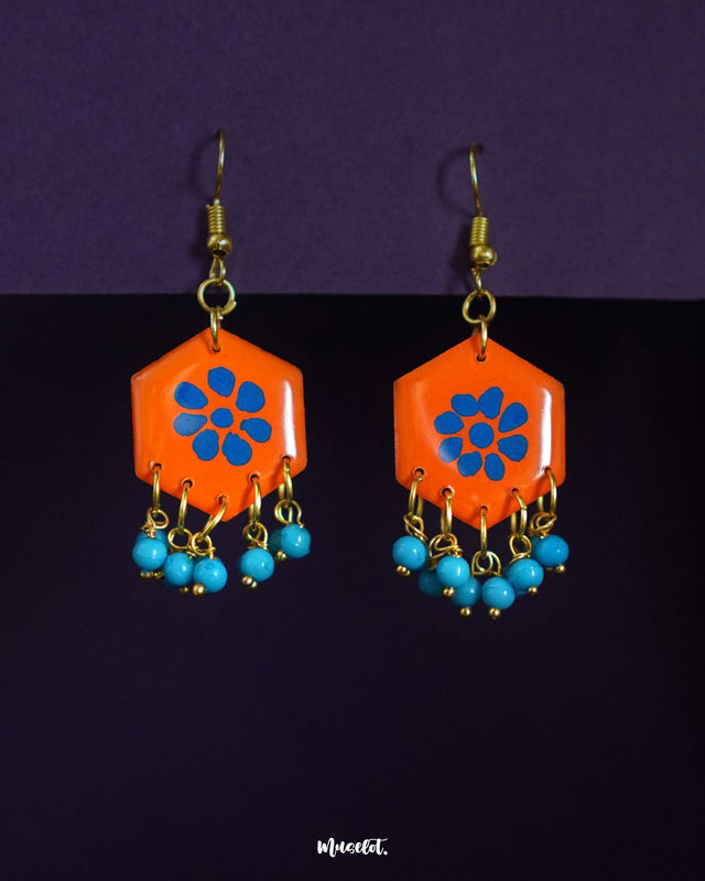 Surkhshaam orange floral hook earrings, set against a warm, neutral backdrop, with vibrant blue petals and intricate floral detailing that add a bold yet elegant touch to any look — Muselot.