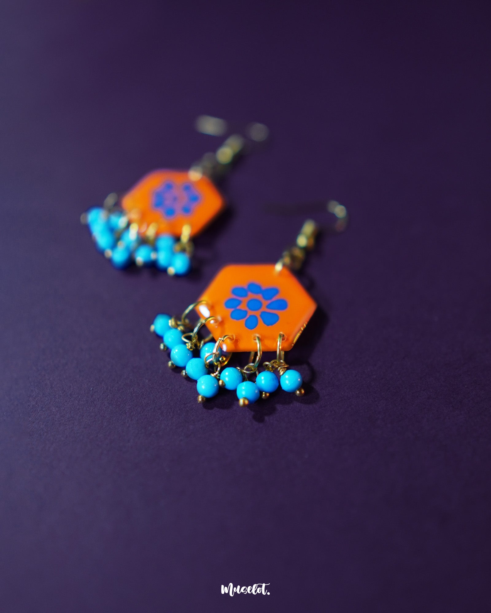 Surkhshaam orange floral stud drop earrings, set against a deep purple background, featuring vibrant blue floral accents and a graceful drop design that beautifully combine boldness and elegance — Muselot.