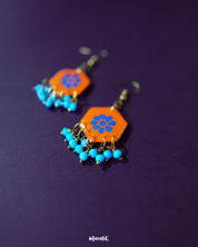 Surkhshaam orange floral stud drop earrings, set against a deep purple background, featuring vibrant blue floral accents and a graceful drop design that beautifully combine boldness and elegance — Muselot.