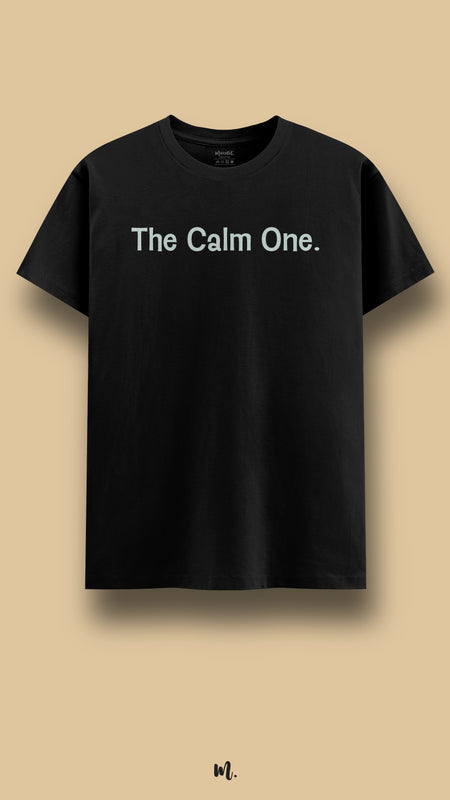 Black graphic t-shirt showcasing the statement “The Calm One.” in muted mint typography, highlighting a composed, steady, and balanced personality against a clean beige background – Muselot