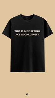 Black graphic t-shirt showcasing the “This Is Me Flirting. Act Accordingly.” statement, highlighting a cheeky, self-assured vibe perfect for statement streetwear,showcased against a clean, minimal beige background – Muselot