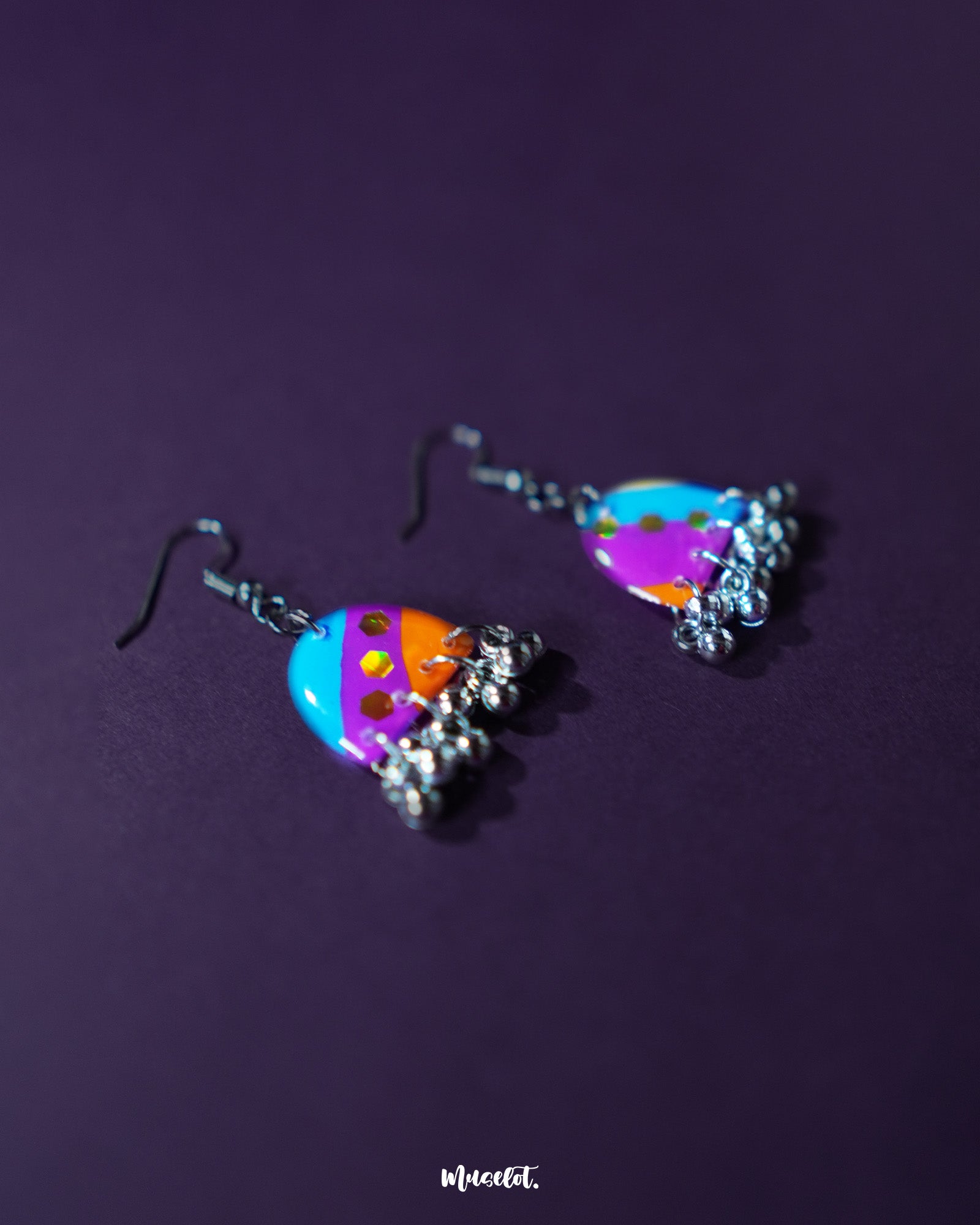 Ufaq multicolor hook earrings, placed against a dark purple background, featuring an explosion of vibrant hues and intricate patterns that enhance their bold yet elegant look — Muselot.