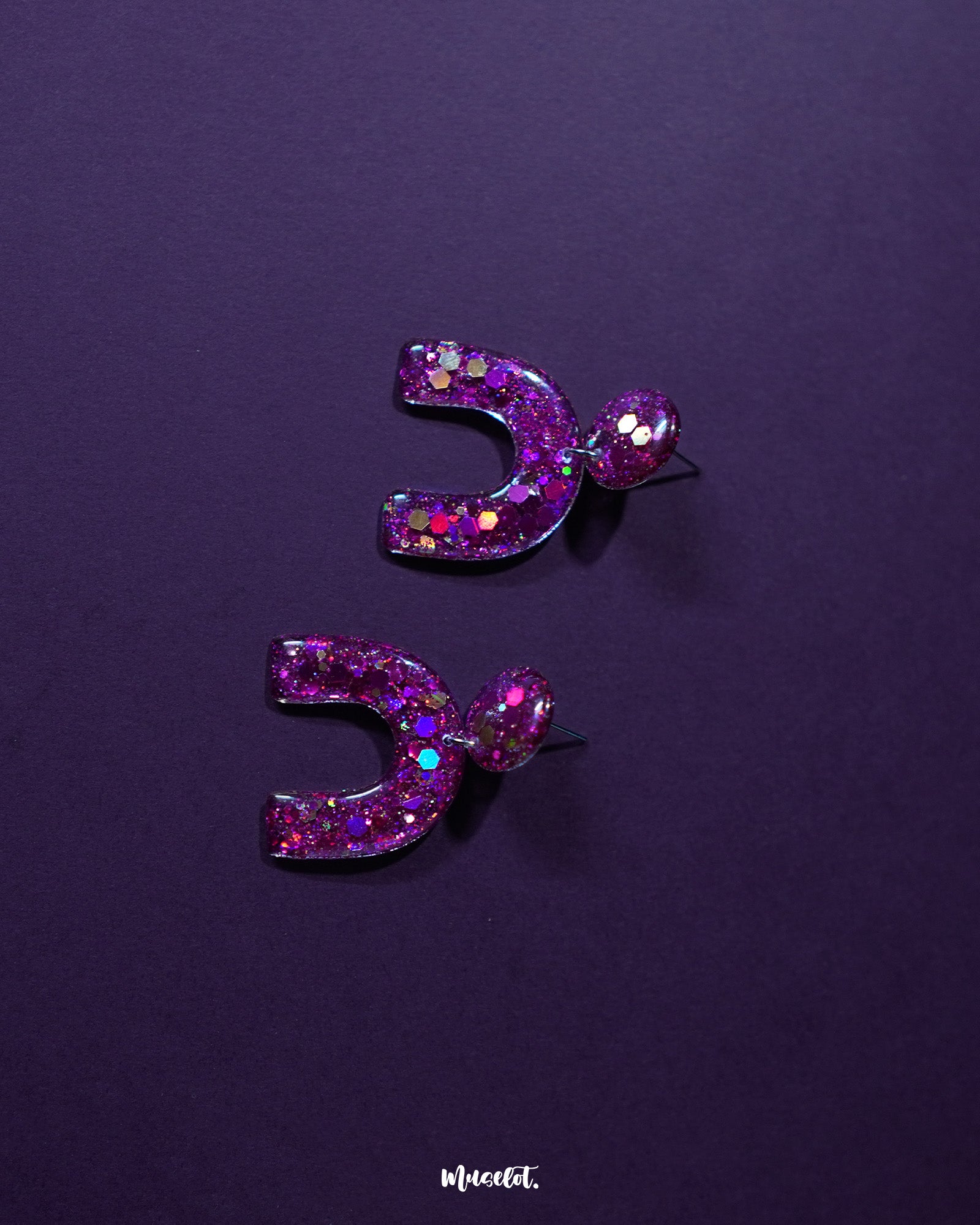 Front display of Ulfat glitter stud earrings, featuring bold arch-shaped resin design with pink and purple sparkles on a clean backdrop – Muselot.