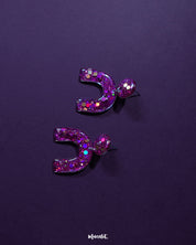 Front display of Ulfat glitter stud earrings, featuring bold arch-shaped resin design with pink and purple sparkles on a clean backdrop – Muselot.