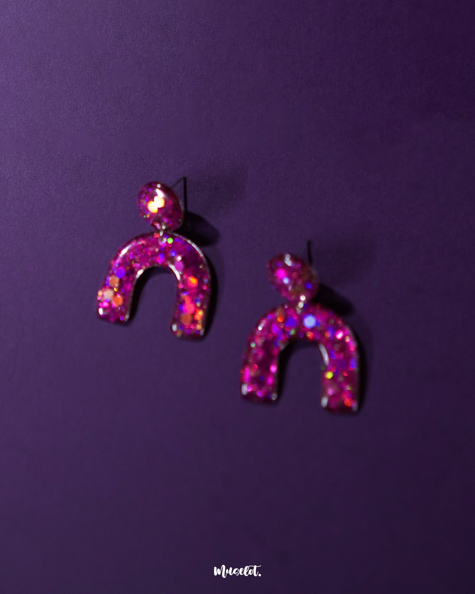Close-angle shot of Ulfat glitter stud earrings, showcasing the resin texture and vibrant pink-purple sparkle within the bold arch shape – Muselot.