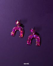 Close-angle shot of Ulfat glitter stud earrings, showcasing the resin texture and vibrant pink-purple sparkle within the bold arch shape – Muselot.