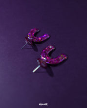 Ulfat glitter stud earrings displayed upright, showcasing the arch silhouette and vibrant pink-purple glitter blend against a simple backdrop – Muselot.