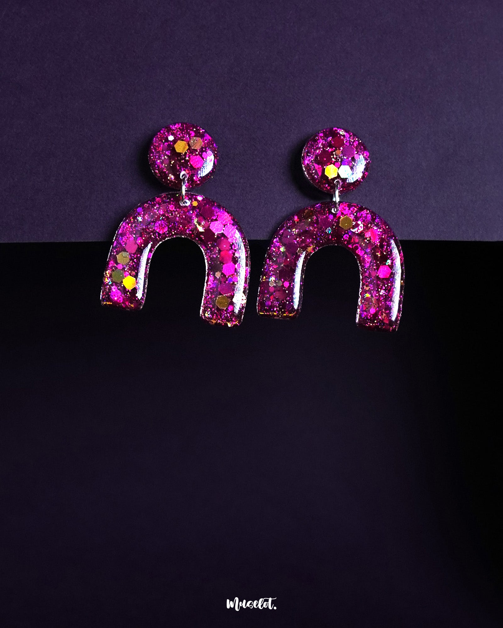 Ulfat glitter resin stud earrings in vibrant pink-purple hues, featuring a bold arch shape adorned with chunky sparkles, displayed on a dark background – Muselot.