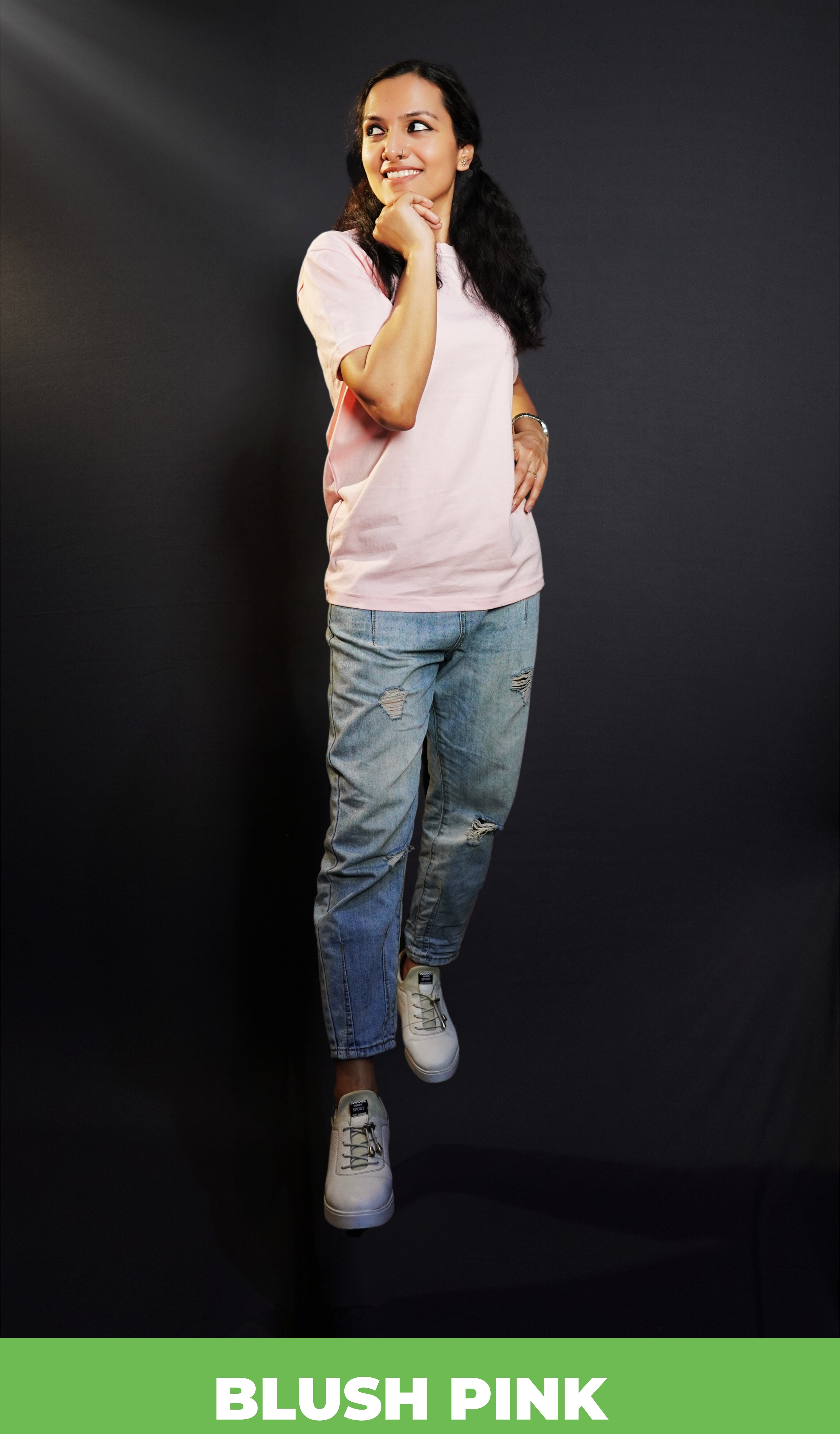 A stylish model wearing a blush pink plus size plain round neck stretchable t shirt, posing with her hand softly curling under her chin and other on her waist as she looks sideways, showcasing a trendy baggy fit-Muselot