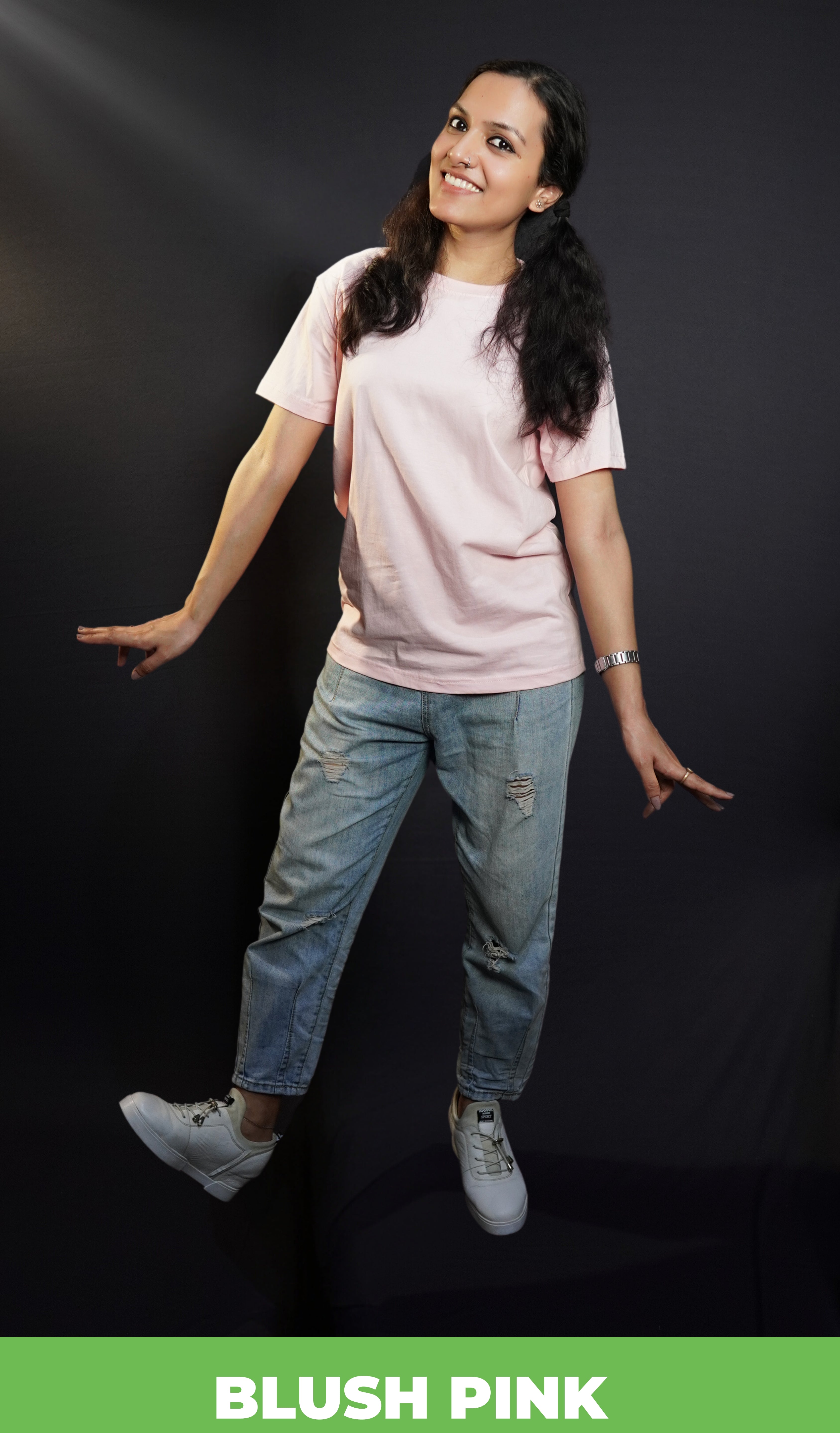 A stylish model happily poses in a plain, casual blush pink t-shirt with cheerful expression and fun pose complementing the simple, versatile top, highlighting a cool easy fit-muselot