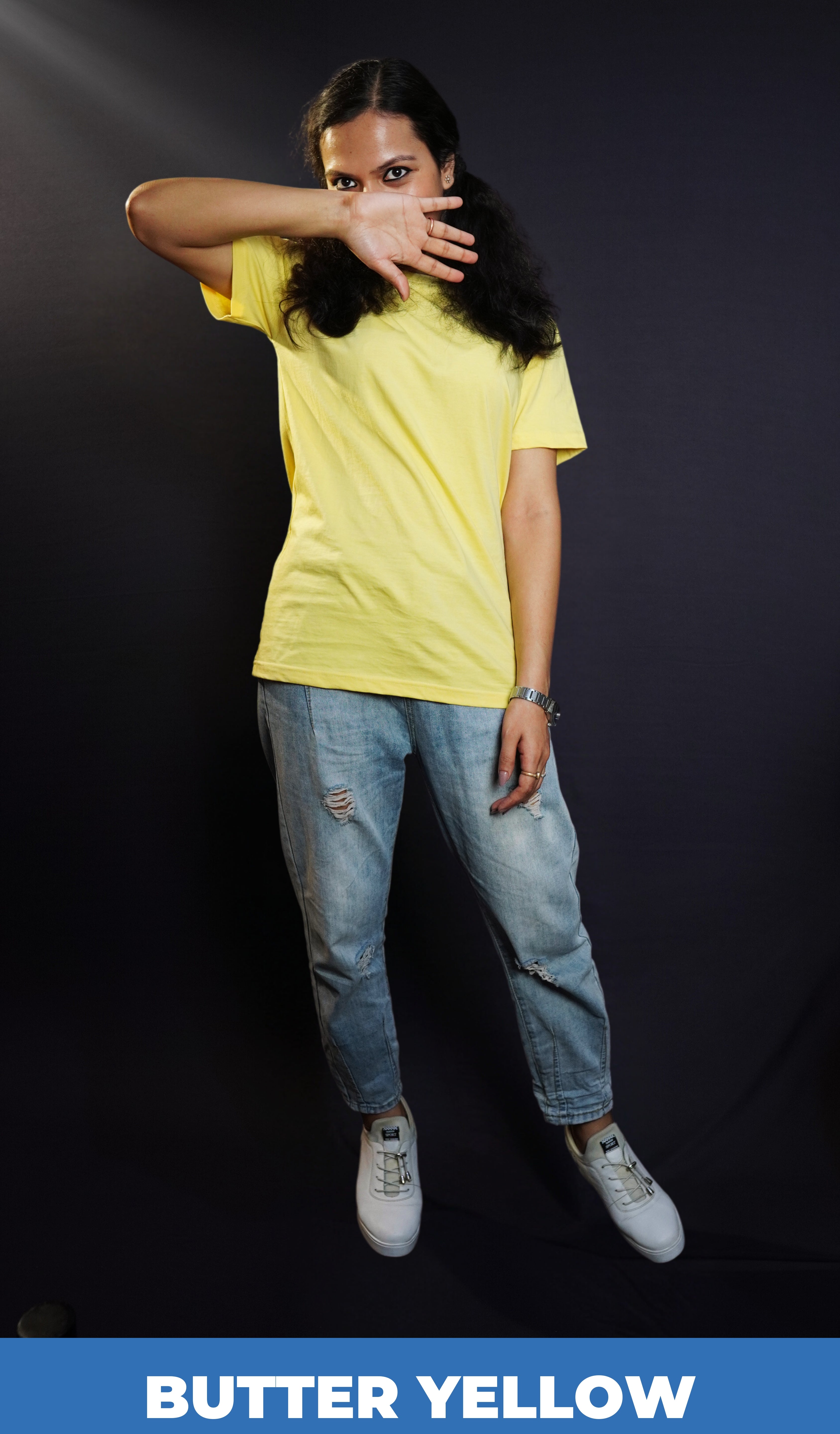 A woman wearing a round neck short sleeved long length moisture wicking butter yellow t-shirt, posing with her hand covering half of her face and sparkling eyes looking at the camera, highlighting a casual modern fit-Muselot