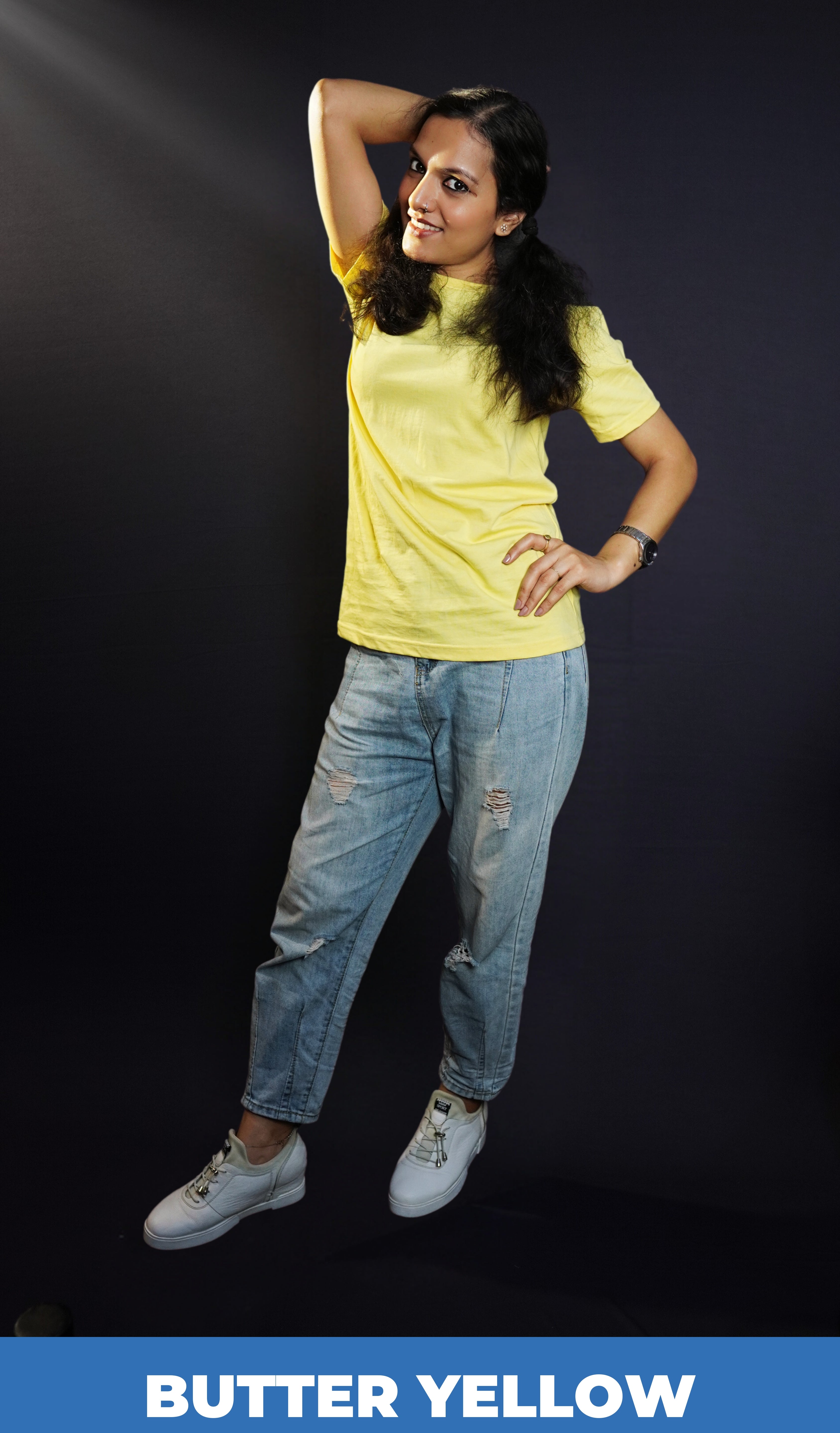 A woman wearing a plain cotton summer butter yellow t-shirt, posing with her hand on her waist and another behind the back of her head, showcasing a trendy voguish look-Muselot
