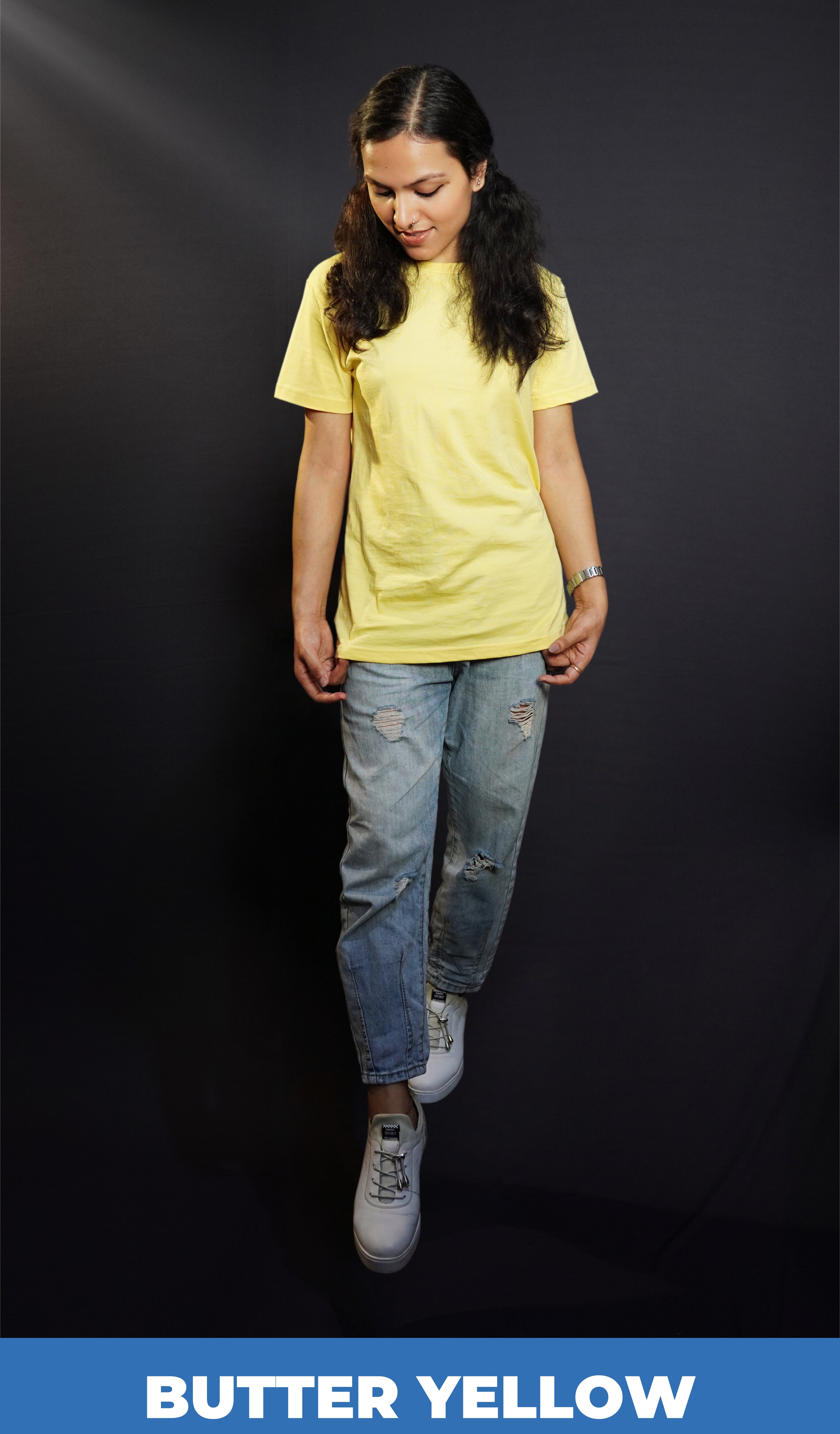 a stylish model wearing a butter yellow plain stretchable t-shirt, standing with her head slightly bent down and her hands grabbing the side of the t-shirt, showcasing an elegant casual fit-Muselot