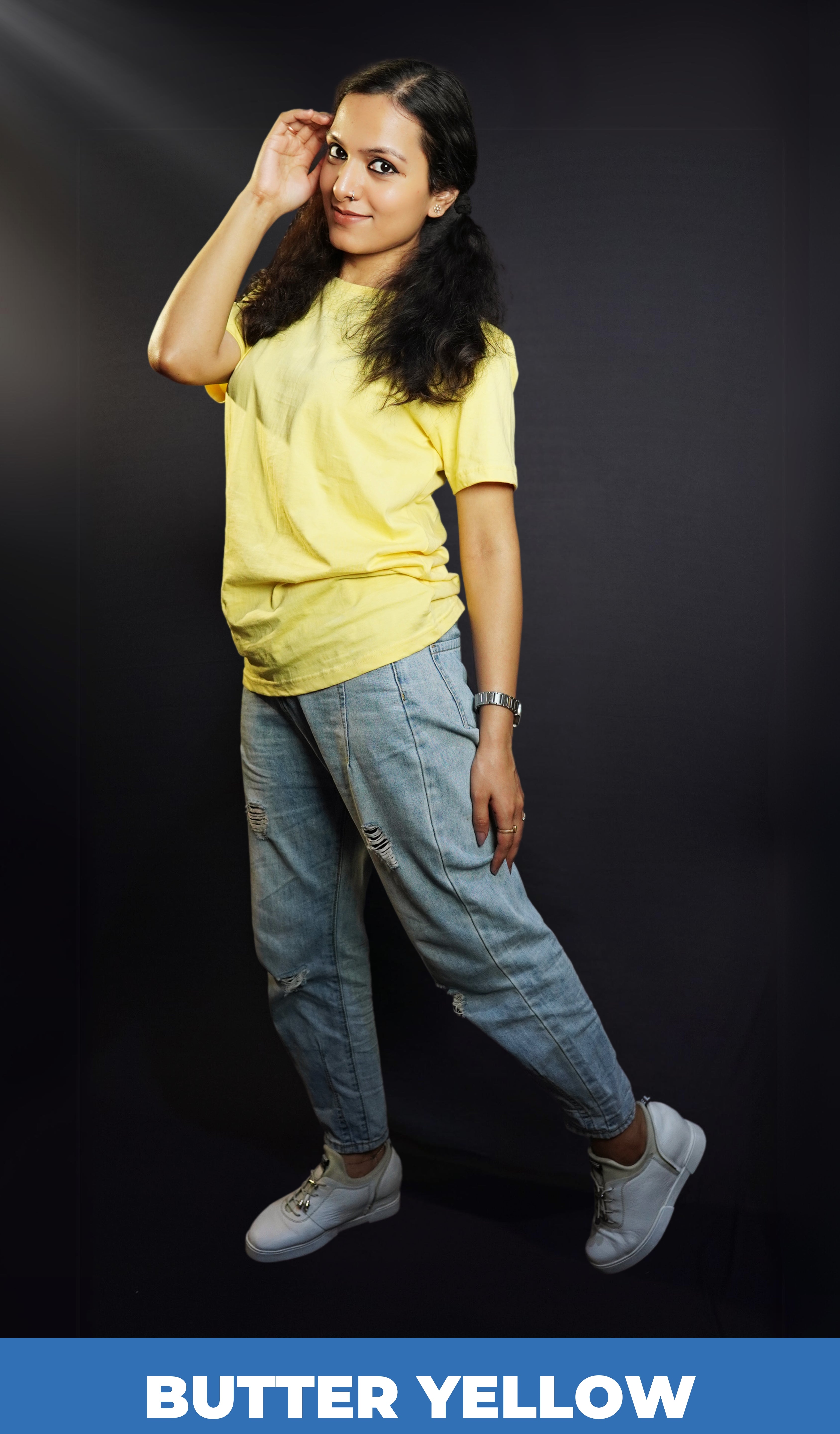 A woman wearing a butter yellow unisex quick drying t shirt, posing with her hand at the side of her head as she stands sideways, showcasing a stylish modern look-Muselot