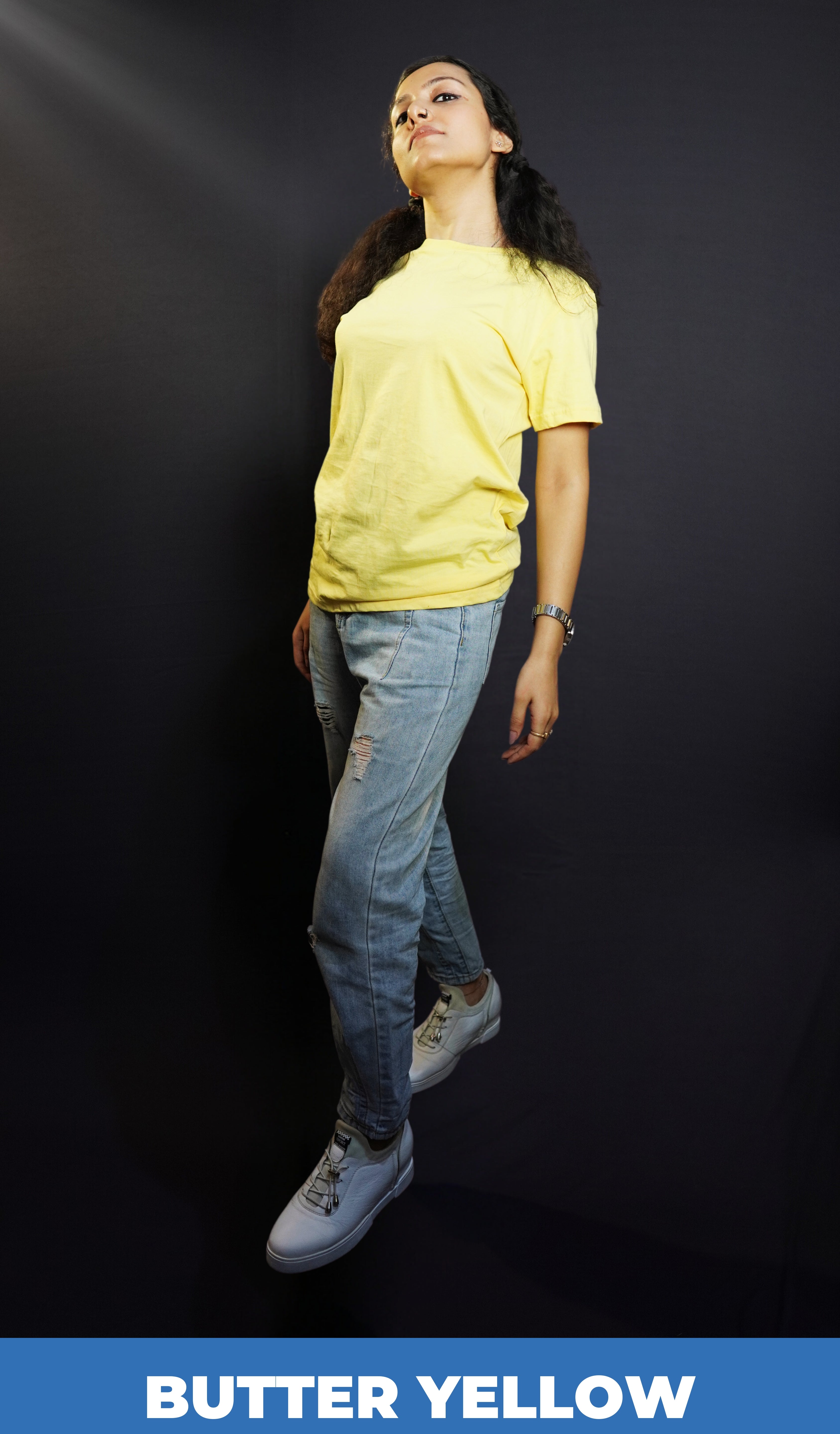 A woman posing as she slightly bends backward with her one leg in front of another, wearing a plain cotton women's round neck butter yellow t-shirt, highlighting a relaxed swank style-Muselot
