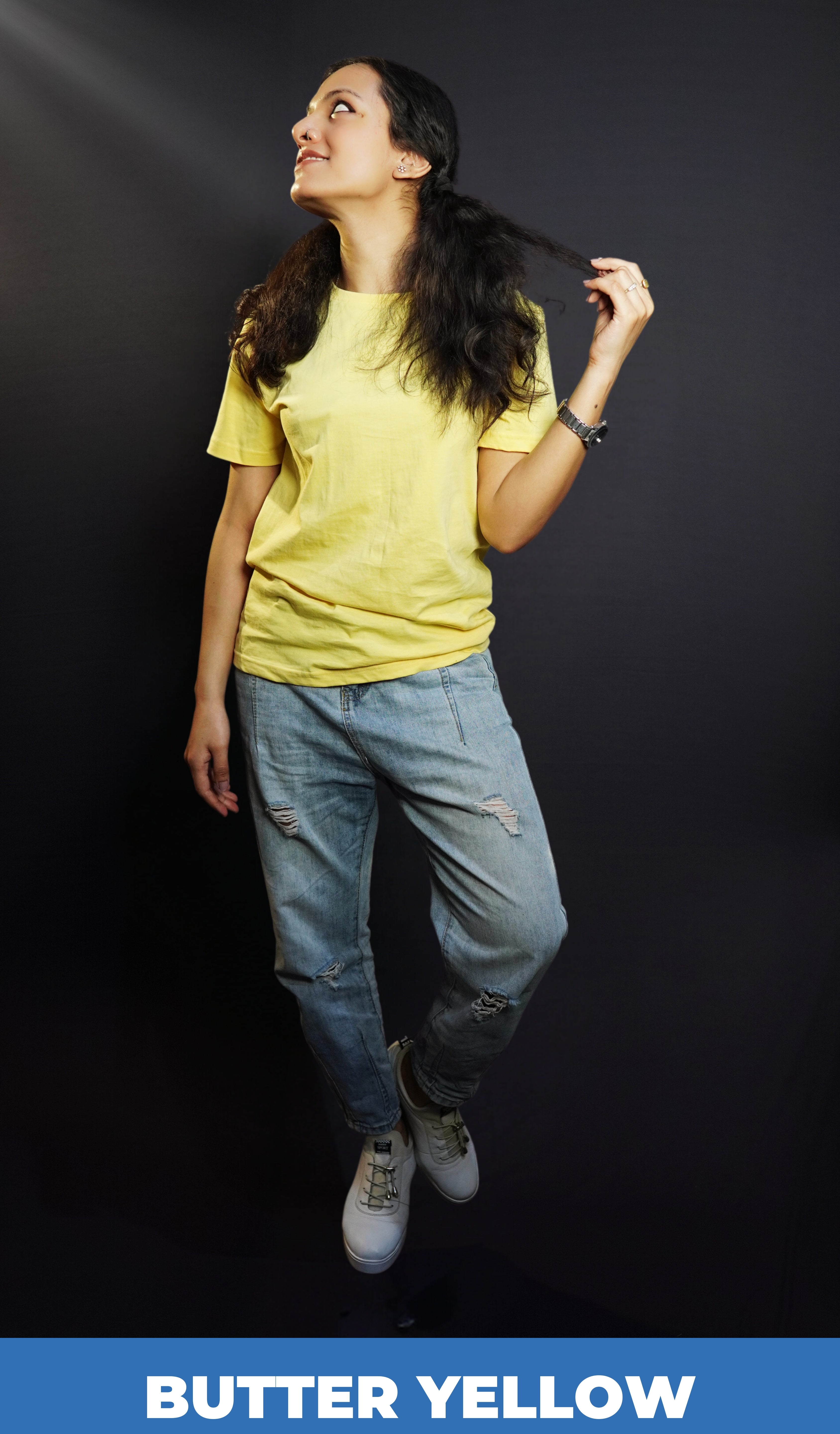 A woman wearing a butter yellow men's round neck long length t-shirt, posing with her hand pulling the tip of her hair as she looks sideways, showcasing an up to the minute baggy fit-Muselot