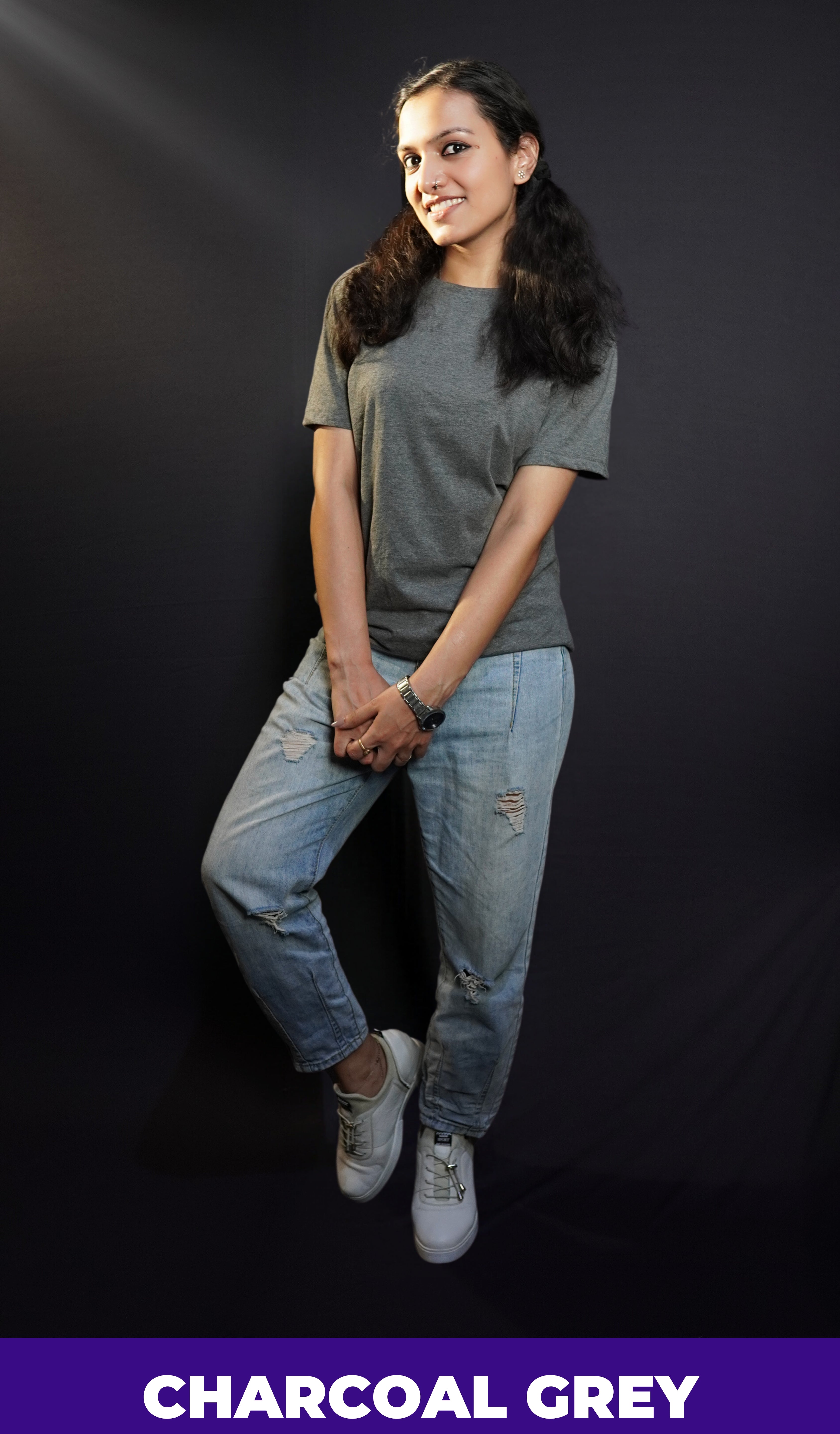 a woman with a smile on her face wearing long length t shirt pairing with ripped jeans and white shoes and a silver watch around her wrist-muselot