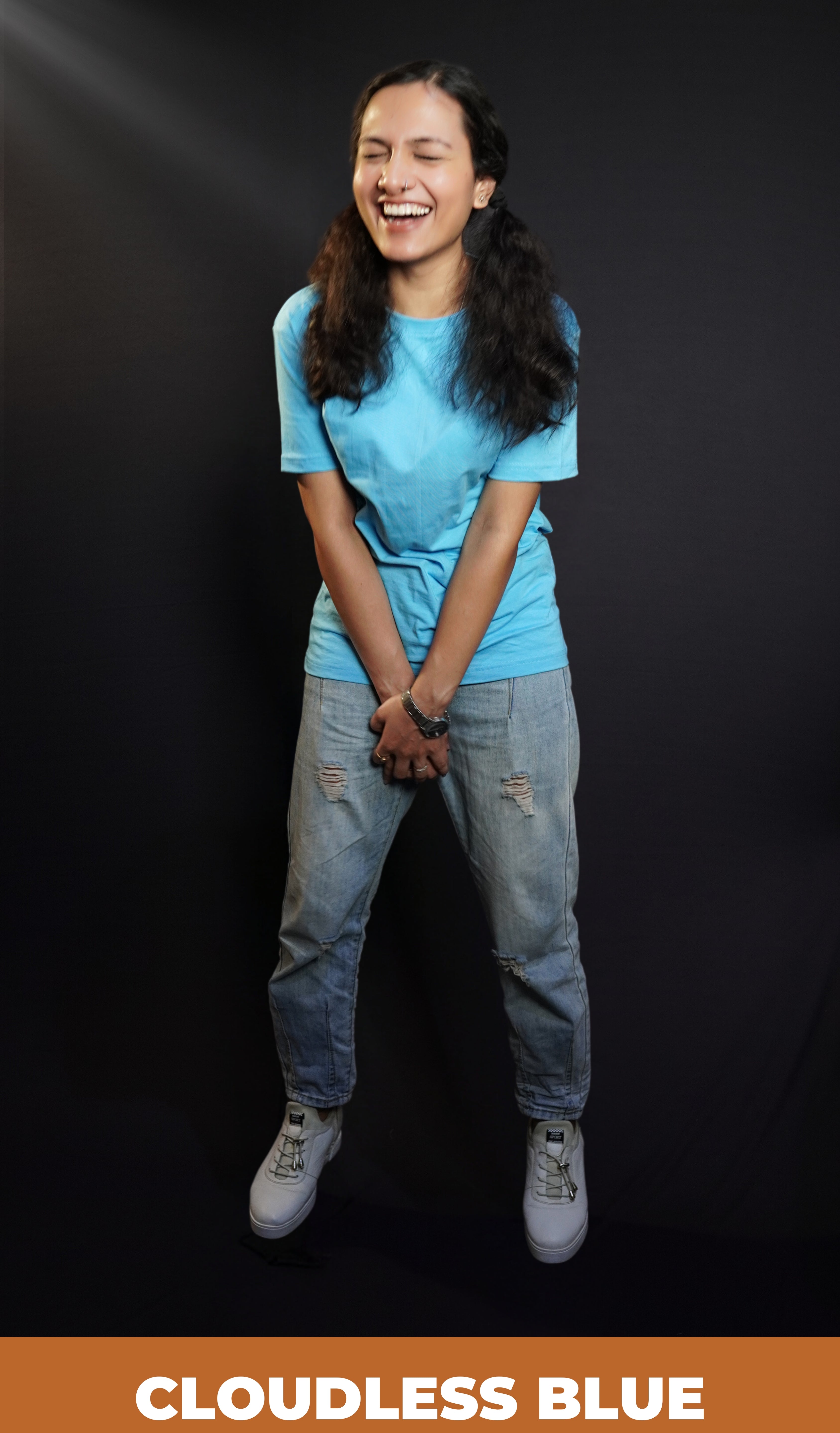 A woman wearing a plain long length cloudless blue t shirt holding her both hands as she laughs out loud, highlighting a casual easy fit-Muselot