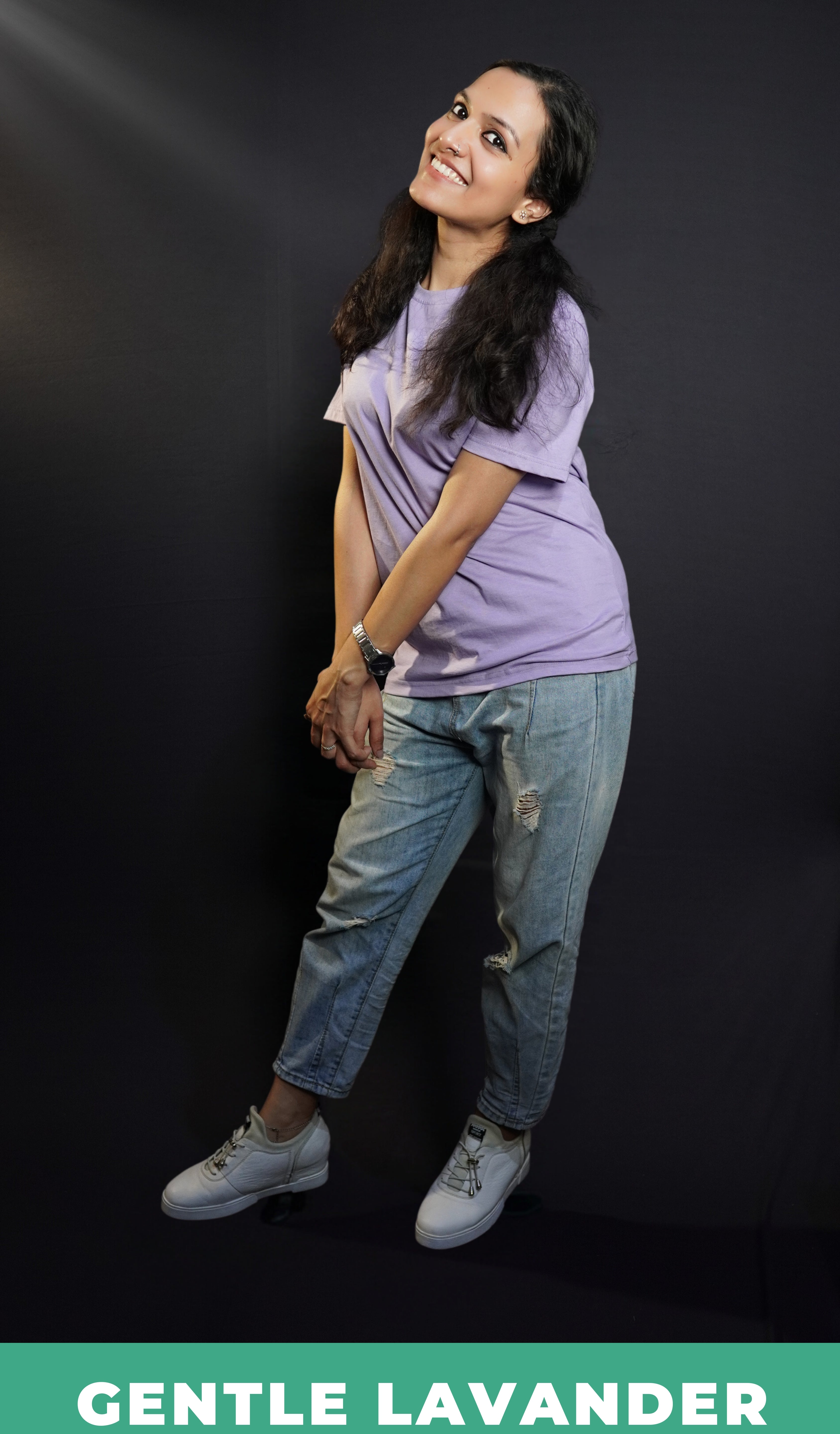 A woman standing sideways against a dark background in a men's cotton stretchable t-shirt, posing by grabbing her hands together, highlighting a popular casual fit-Muselot