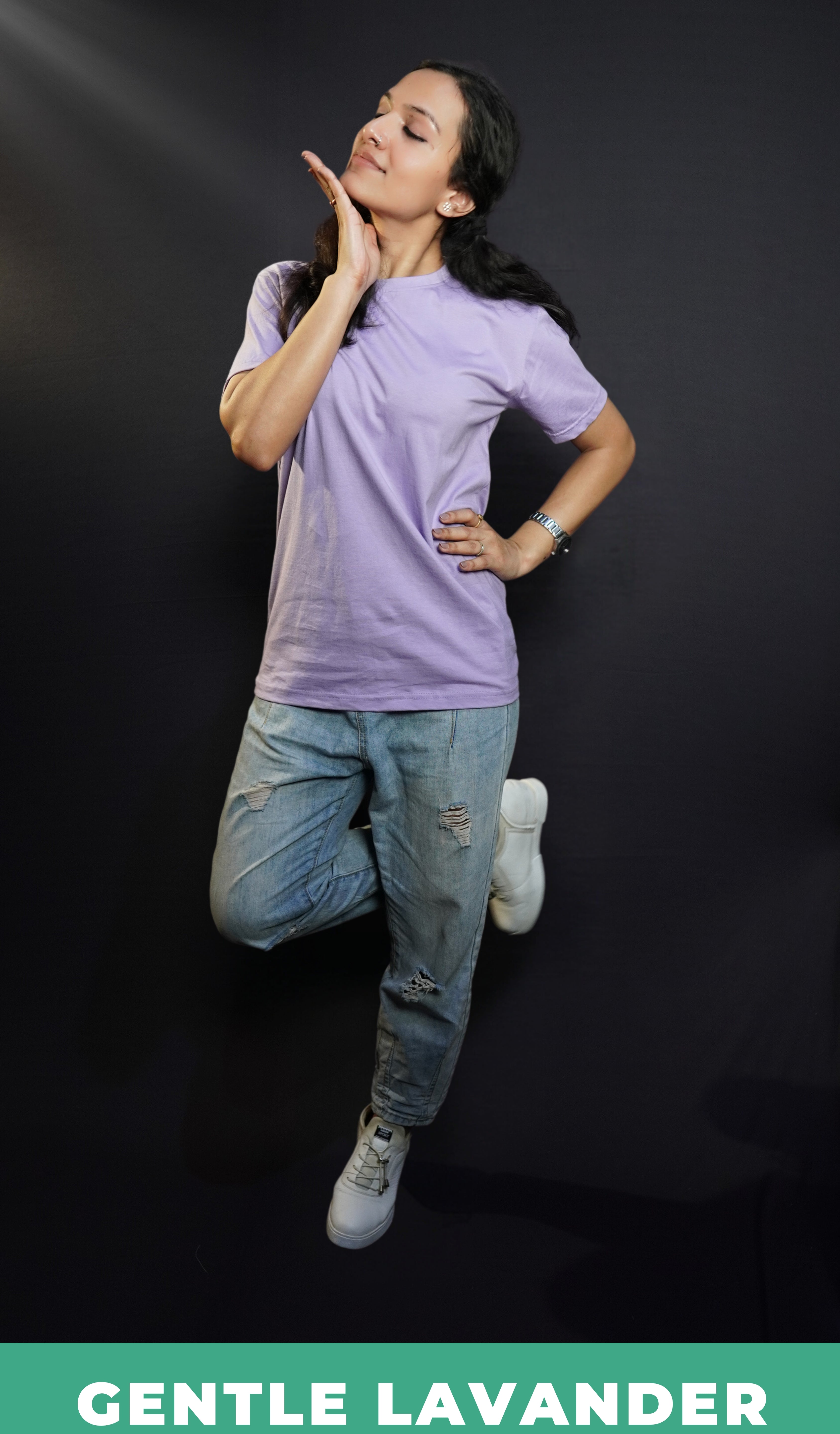A stylish model posing with her hand sideway and below her chin, wearing a long length cotton plain round neck gentle lavender t-shirt, showcasing a flowing modish style-Muselot